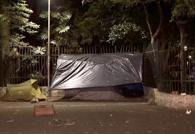 Abrigo improvisado, com lonas de plástico, em calçada, durante a noite