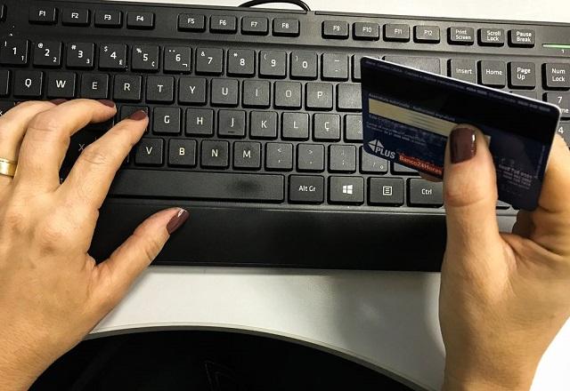 Pessoa segura cartão com uma mão e digita em teclado com a outra (Marcello Casal Jr./Agência Brasil)