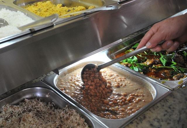 Pessoa utiliza concha para pegar feijão em recipiente, em restaurante (Antonio Cruz/Agência Brasil)