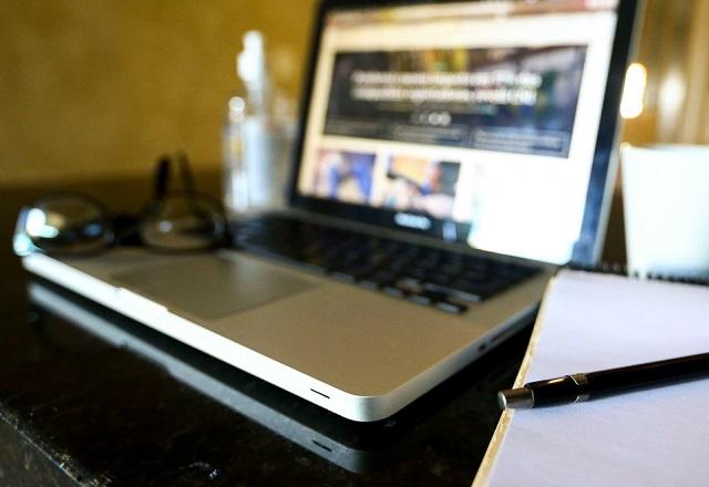 Óculos sobre laptop ao lado de caderno e caneta, em mesa (Marcelo Camargo/Agência Brasil)