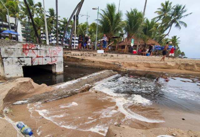 Água preta saindo de uma galeria de esgoto com mau cheiro e correndo pela areia da praia até encontrar com água do mar