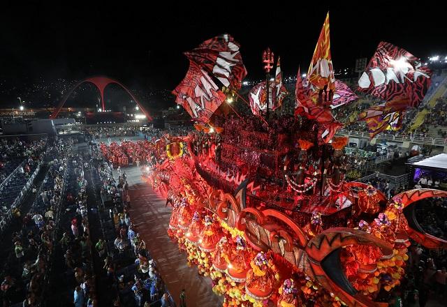 Alegoria de escola de samba em tom vermelho, com várias bandeiras tremuladas, passando na passarela de desfile
