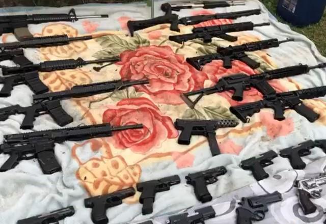 Armas, como fuzis, pistolas e revólveres, expostas em cima de um lençol sobre o chão