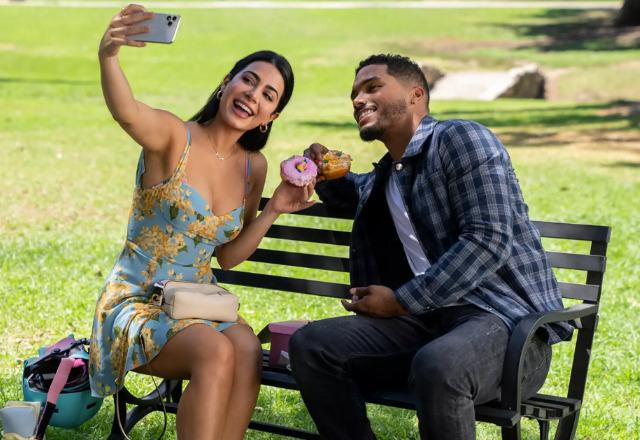 Atores da série ''Com Amor'' sentados num banquinho de parque tirando uma selfie com doces
