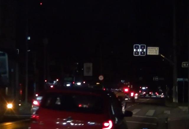 Avenida sem luz, durante a noite, com faróis de veículos ligados durante o tráfego