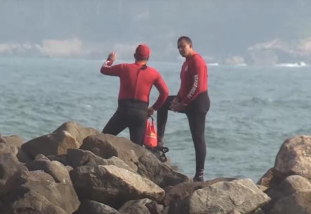 Bombeiros em uma pedra ao lado do mar