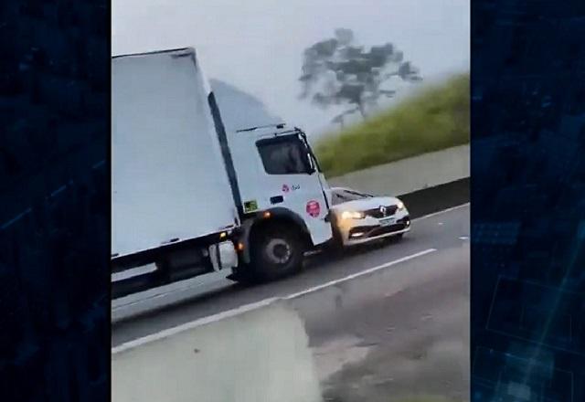 Caminhão arrastando veículo preso no para-choque, em rodovia