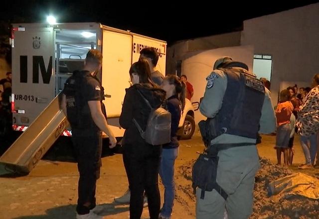 Caminhão do IML ao lado de cena de crime, com movimentação de policiais fardados e pessoas, durante a noite