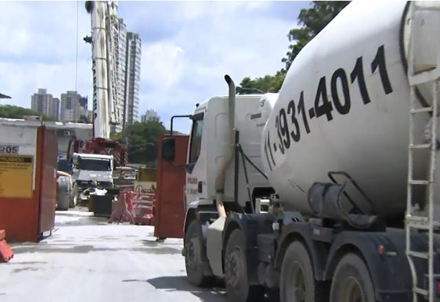 Caminhão do tipo betoneira entrando em garagem de obra, durante o dia, visto pela parte traseira