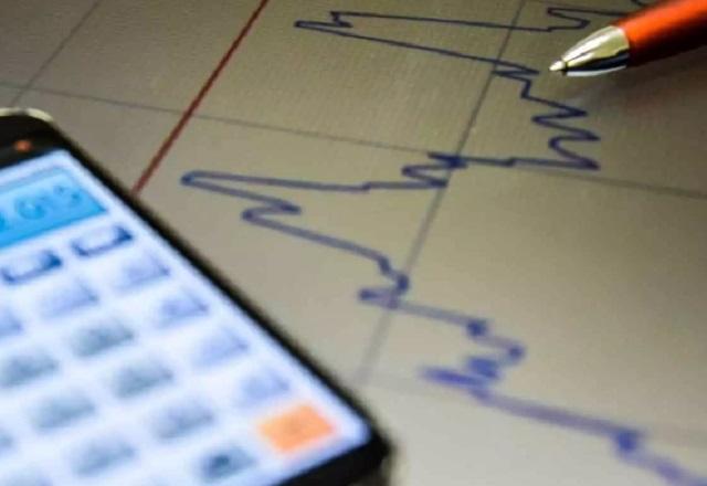 Caneta e celular com calculadora sobre folha com gráfico (Agência Brasil)