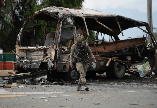 Militar caminha ao lado dos destroços do ônibus-bomba em Villa Rica, na Colômbia | Foto: Ernesto Guzmán