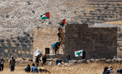 Ativistas palestinos e israelenses se protegem de disparos de colonos em Beit Sahour, na Cisjordânia, em 14 de agosto. REUTERS/Mussa Qawasma