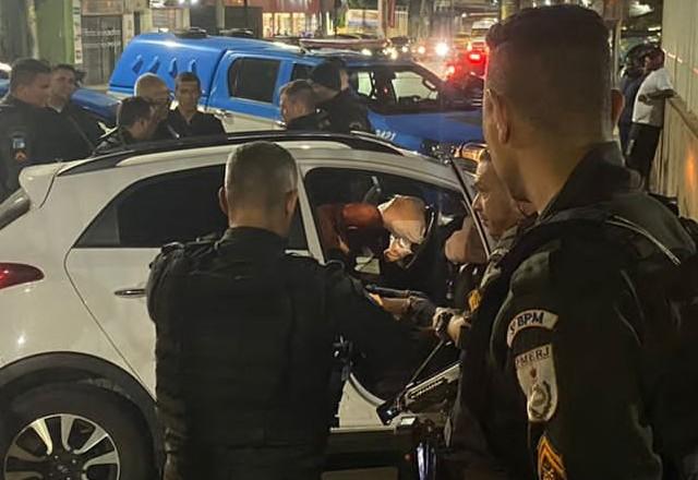 Carro branco com um homem dentro e diversos policiais ao redor