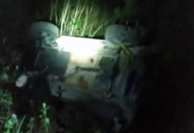 Carro despencando em barranco, com os pneus para o alto, em área de mata