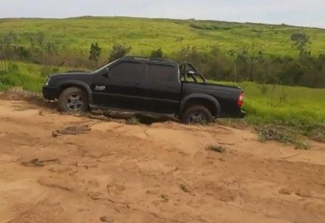 Carro tipo caminhonete atolado em estrada de terra, ao lado de matagal