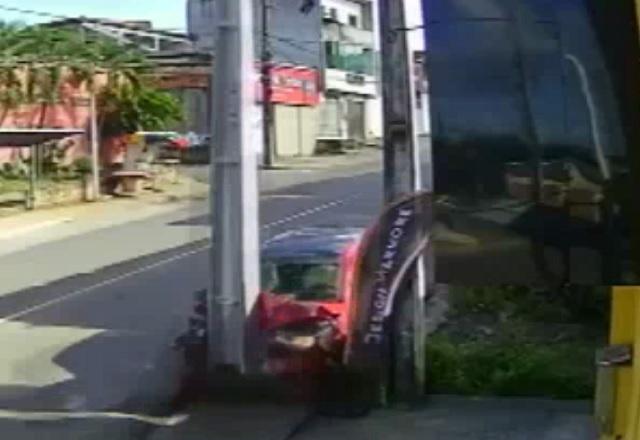 Carro vermelho destruído após bater em poste, em rua, durante o dia