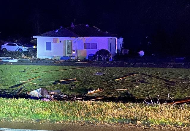 Casa destruída após passagem de tornado, com destroços ao redor, durante a noite