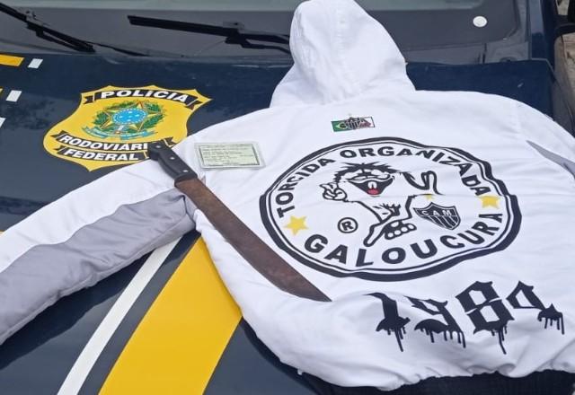 Casaco com capuz em cima de uma mesa e facão em cima do casaco