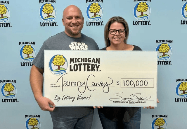 Tammy Carvey e o marido posam ao lado de cheque de US$ 100 mil (R$ 573,4 mil), valor que ela ganhou na Powerball, a loteria dos EUA | Foto: Divulgação/Loteria de Michigan