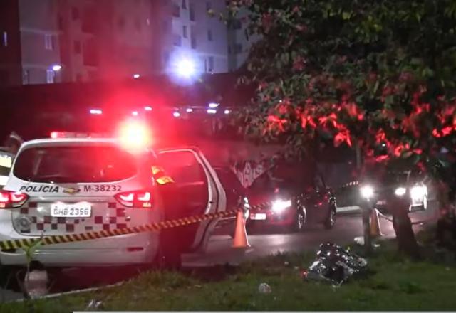 Corpo coberto no chão ao lado de viatura da polícia