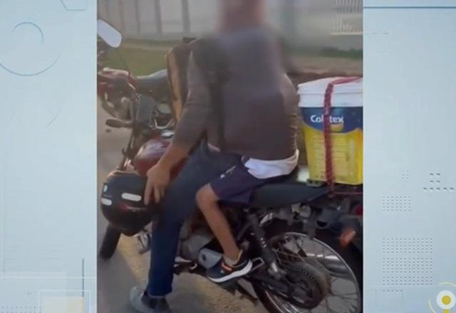 Criança dentro de camiseta de piloto de moto, com os dois sobre o veículo, em rodovia durante o dia