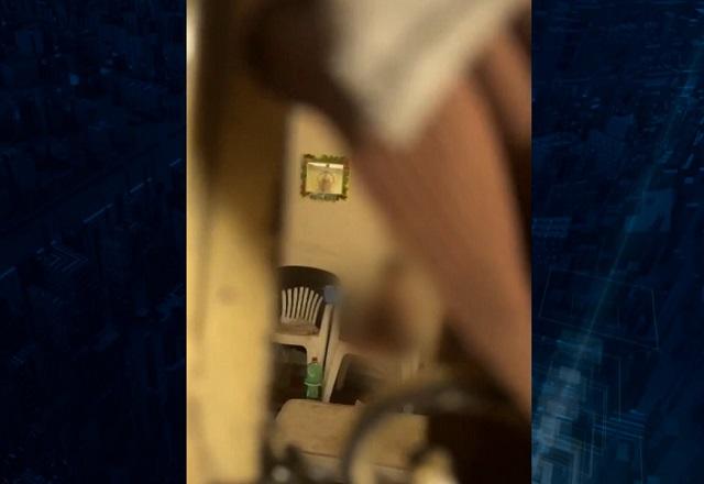 Criança sem ser identificada, ao fundo, vista por buraco em janela, dentro de sala de apartamento