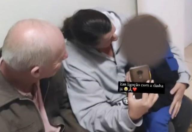 Criança sentada no colo da avó, ao lado do avô