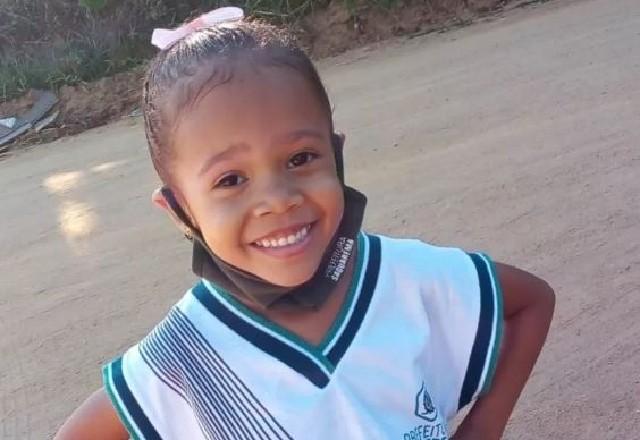 Criança sorrindo com mãos na cintura, vestida com uniforme escolar