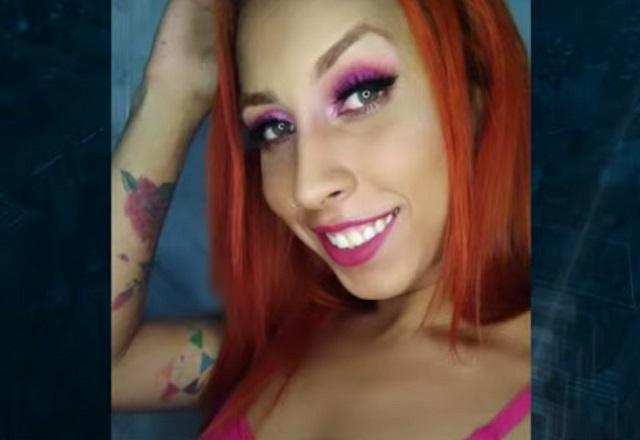 De cabelo ruivo e blusa rosa, modelo trans lorena muniz sorri para foto com a mão na cabeça