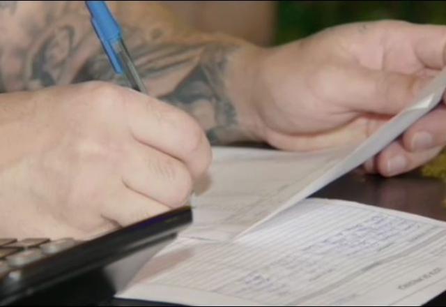 Detalhe da mão de uma empresária segurando uma caneta e com papéis referentes às contas do negócio dela.