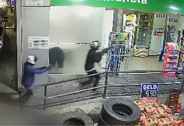 Dois homens com armamento pesado correndo na direção de loja de conveniência de posto de combustíveis