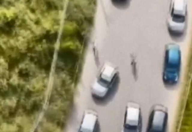 Dois homens correndo no meio de rodovia movimentada, com carros