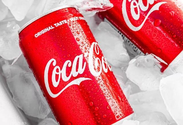 Duas latinhas de Coca-Cola; elas são vermelhas com o nome da marca escrito em branco