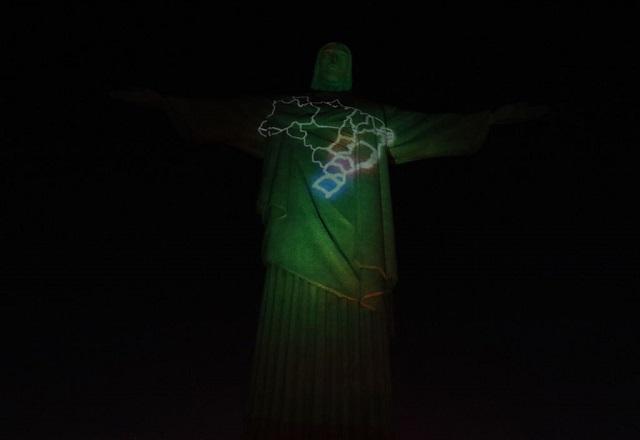 Estátua do cristo redentor às escuras, com projeção do mapa do brasil no peito do monumento