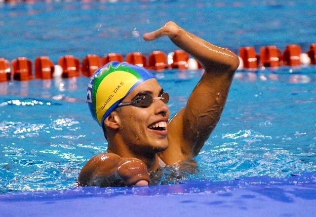 Foto de Daniel Dias em uma piscina. Ele está de touca e óculos de natação, sorrindo e comemorando