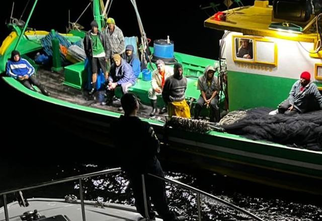 Foto de uma embarcação no mar, a noite, com vários homens dentro