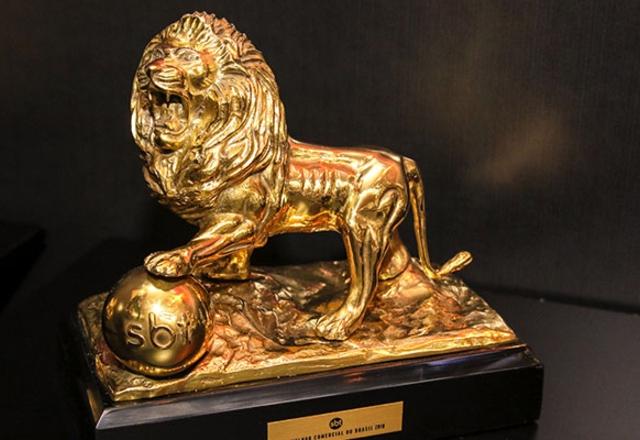 Foto de uma estatueta dourada de um leão. Ele parece estar rugindo e repousa a pata dianteira esquerda em um globo, que representa o símbolo do SBT