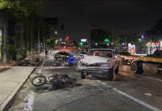Foto geral noturna mostrando moto incendiada, guincho, carro da polícia, posto de combustíveis e vários luminosos verdes ao fundo