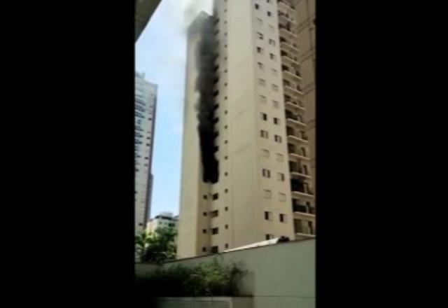 Fumaça preta saindo de janela de apartamento de prédio, durante o dia