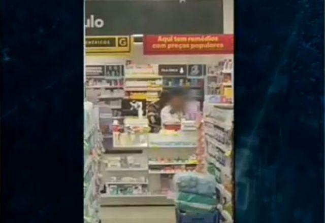 Funcionário sendo mantido refém com uma arma na cabeça segurada pelo criminoso dentro da farmácia, atrás do balcão