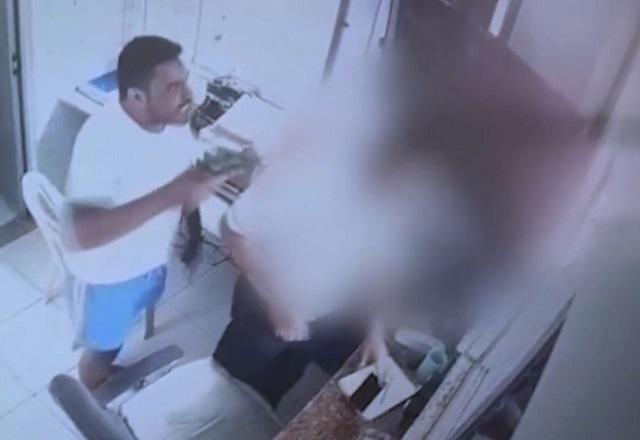Homem armado, de camiseta branca, apontando para porteiro dentro de portaria de prédio