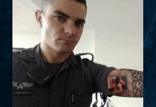 Homem branco, com braço tatuado com desenhos de caveira, usando uniforme cinza da polícia militar de são paulo