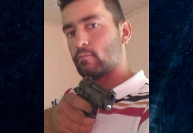 Homem branco, de cabelos e barba escuros, apontando arma para a foto