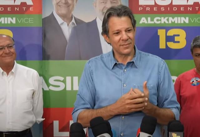 Homem branco, de camisa azul, falando em púlpito com microfones durante entrevista