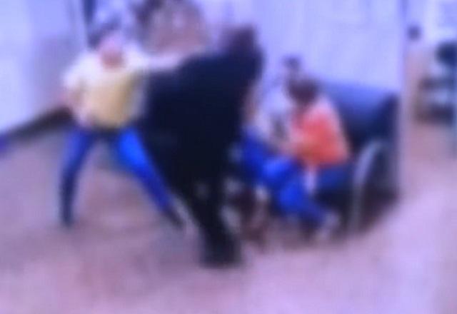 Homem branco de camiseta amarela, armado e agredindo homem negro de terno, em recepção de hospital