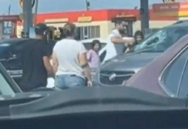 Homem branco quebrando para-brisa de carro com um soco, durante o dia, em estacionamento