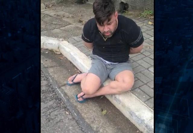 Homem branco sentado em caçada, com as mãos para trás por estar algemado