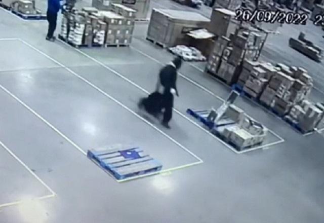 Homem carregando mala e correndo no meio de empresa de logística, aparentando ser um galpão