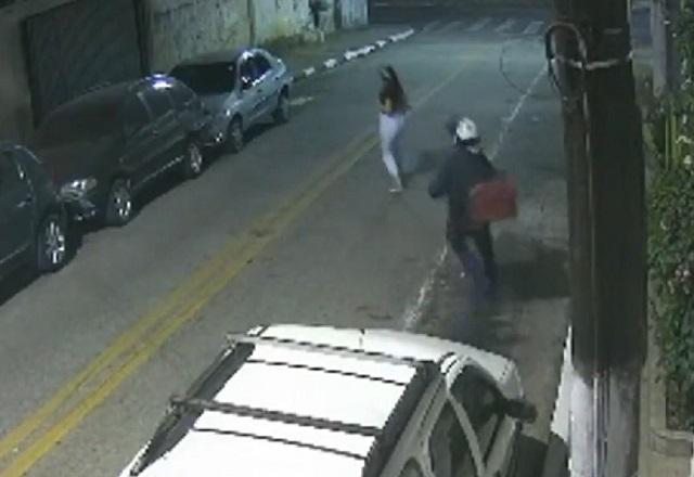 Homem com mochila baú nas costas correndo atrás de mulher, no meio da rua, durante a noite em cena de assalto