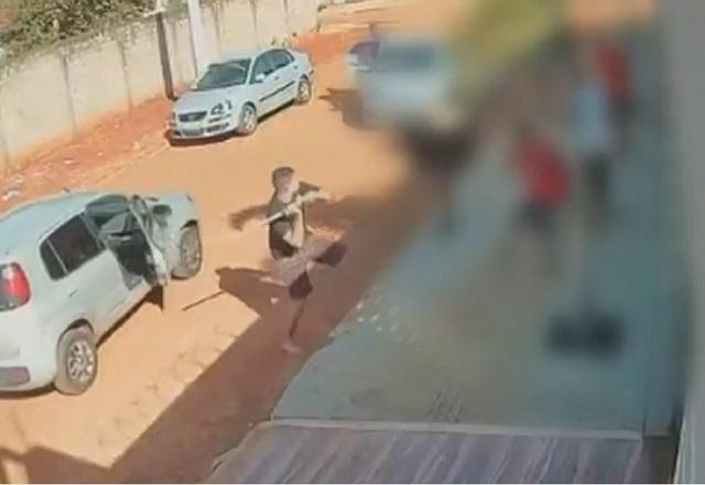 Homem com pedaço de pau desce de carro, em estrada de terra, partindo para agressão a jovens na calçada